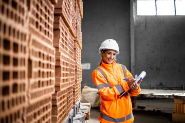 İnşaat alanına teslim etmeye hazır tuğla envanterini kontrol eden bir kadın işçinin portresi..