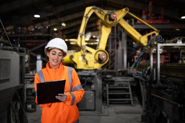 Metal inşaat tesisinde ve arka planda robot kol makinesinde çalışan güzel bir kadın endüstriyel uzman..