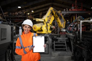 Güvenlik ekipmanı takan ve endüstriyel robot üretim makinesinin önünde duran başarılı kadın işçi..