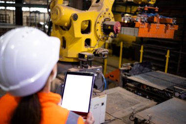 Dijital tablet kullanan ve endüstriyel robot makinesinin verimliliğini kontrol eden güvenlik ekipmanları üreten fabrika mühendisi.