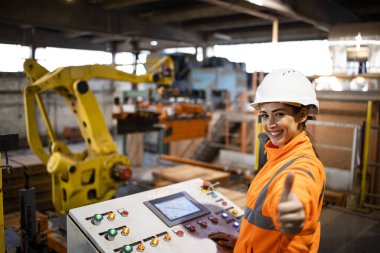 Fabrika işçisi fabrikadaki üretim sürecini başarıyla kontrol ediyor. Arka planda çalışan robot makine.
