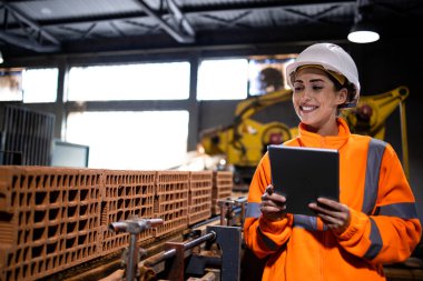 Tablet bilgisayar tutan ve imalat fabrikasındaki işlemin kalitesini kontrol eden üretim hattı kadın çalışanı.