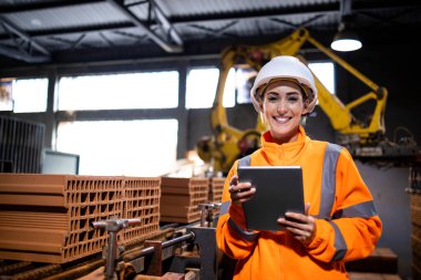 Tablet bilgisayar tutan kadın işçilerin portresi ve üretim fabrikasındaki kil tuğlaların kalitesini kontrol etmek.