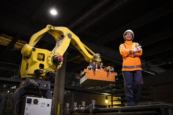 Güvenlik ekipmanları içinde kadın fabrika işçisinin portresi endüstriyel robot makinesinin yanında duruyor ve üretim sürecini izliyor..