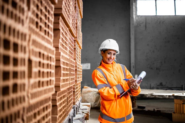 İnşaat alanına teslim etmeye hazır tuğla envanterini kontrol eden bir kadın işçinin portresi..