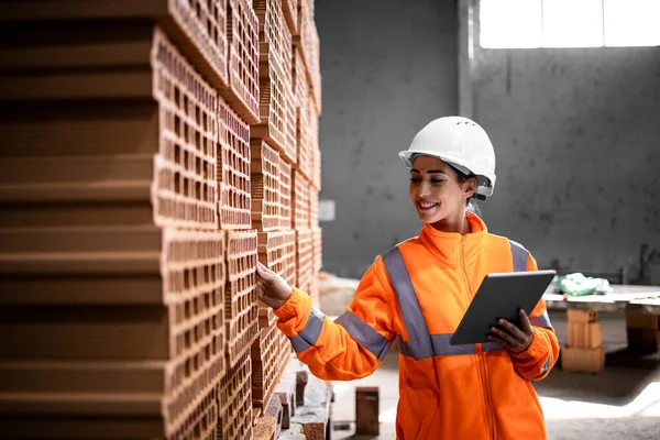 Industrial female worker checking quality of bricks ready to deliver to the construction site.