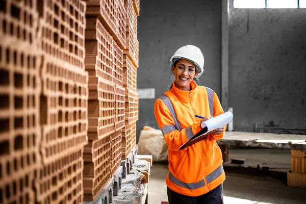 建設現場に納入する準備ができているレンガの在庫を確認する産業女性労働者 — ストック写真