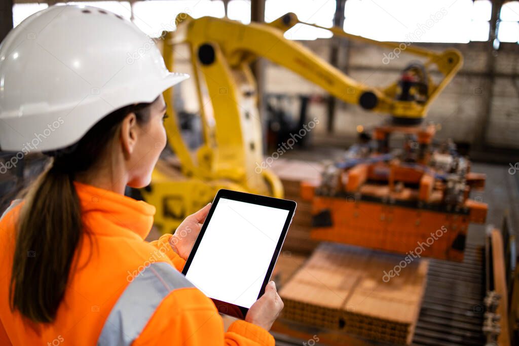 Female worker using digital tablet while supervising production at manufacturing plant.