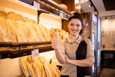 Pasta ve ekmek dolu rafın yanında duran fırın işçisi..