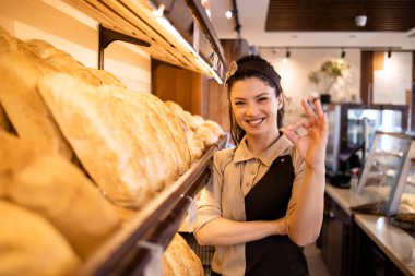 Pasta ve ekmek dolu rafın yanında duran fırın işçisi..
