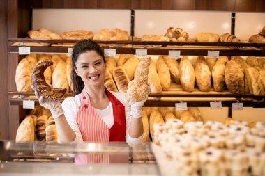 Pozitif gülümseyen fırın işçisi ya da satıcı ekmek dolu rafın önünde taze hamur işi tutuyor..