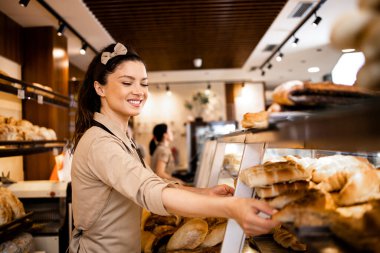Üniformalı güzel kadın şarküteri işçisi taze hamur işleri satıyor ve süpermarket fırınında yetiştiriliyor..