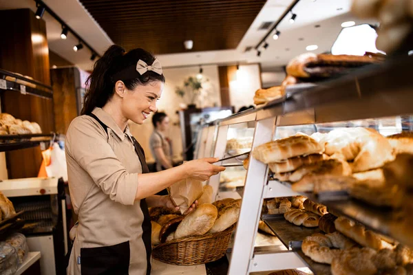 Üniformalı güzel bir şarküteri işçisi taze hamur işleri satıyor ve süpermarket pastanesinde yetiştiriliyor..