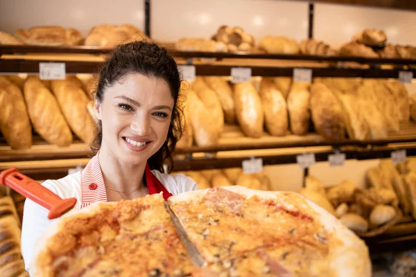 Portrait of supermarket seller holding pizza in bakery department.
