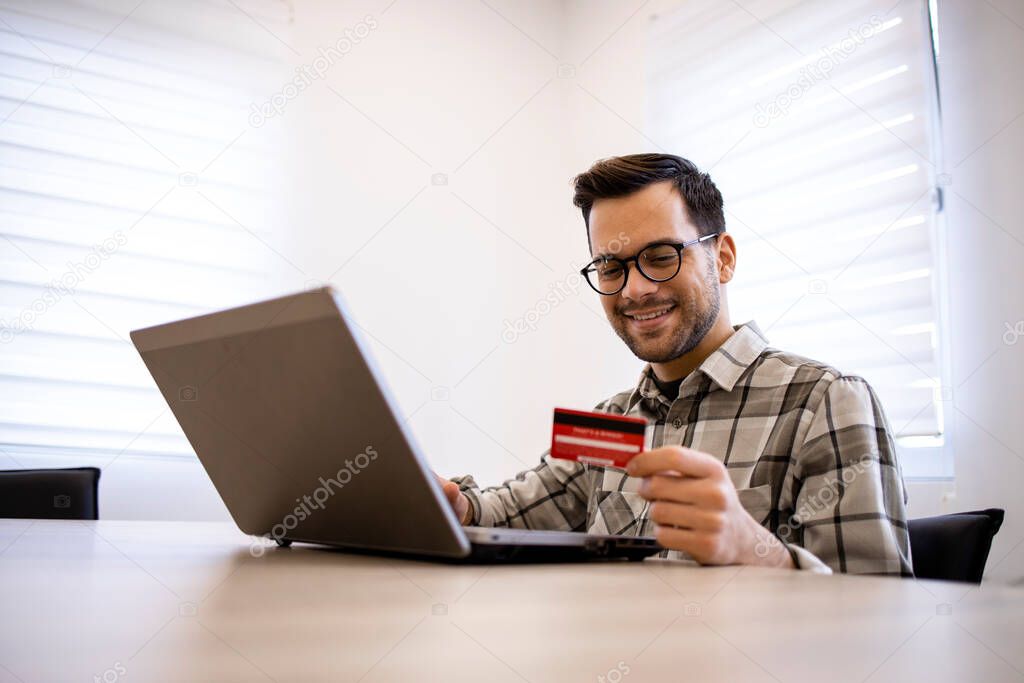 Handsome caucasian man using his laptop computer and credit card for e-banking or purchasing online.