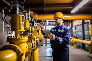 Kafkas mühendisi koruyucu üniforma giyiyor ve fabrikanın içindeki gaz borularını kontrol ediyor..