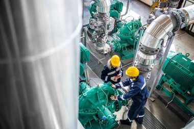 Gaz ve petrol endüstrisi işçileri birlikte çalışıyor ve fabrikadaki boru hattı ve motor pompalarını kontrol ediyorlar..