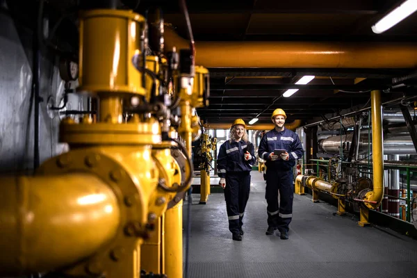 Oil or gas production and industrial engineers walking by gas pipeline inside refinery and checking production.