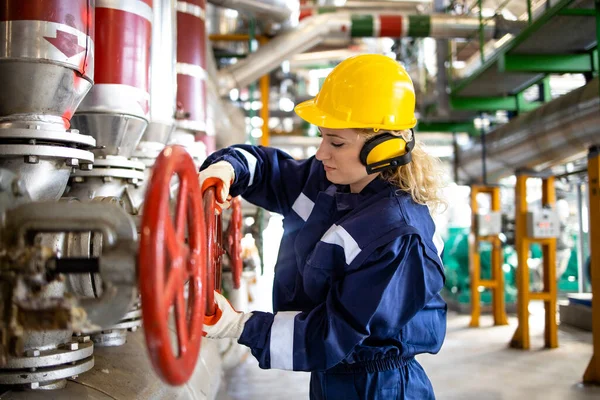 Koruyucu üniformalı profesyonel rafineri işçisi doğal gaz borularının yanında duruyor ve vanayı kapatıyor..