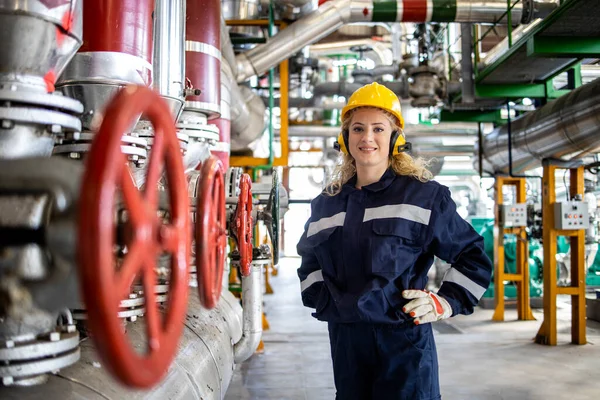 Portrait of female refinery worker standing by gas pipelines in petrochemical factory.
