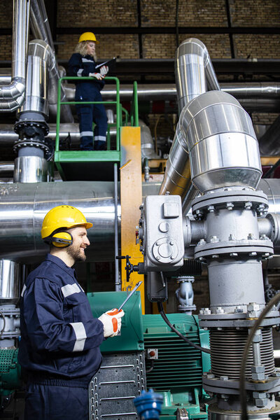 Professional power plant worker checking generator engines and pipeline installations.