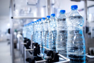 Taşıyıcı banttaki plastik şişeler içme suyu ile dolduruluyor..