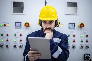 Portrait of thoughtful industrial electrical engineer looking at electric scheme and trying to fix the problem of installation.