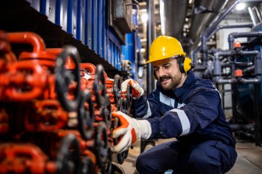 Industrial worker in power plant or heating plant controlling pressure in pipe valves in factory.