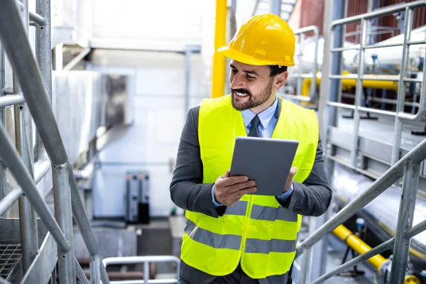 Portrait of young successful manager or supervisor walking through factory production plant and holding computer.