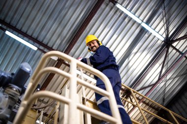 Portrait of factory worker climbing on metal platform in production plant.