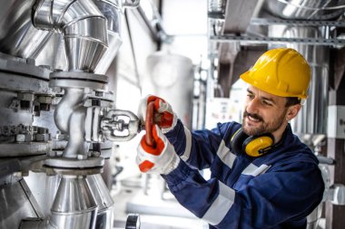 Refinery factory worker closing valve on gas pipeline in petrochemical industrial plant.