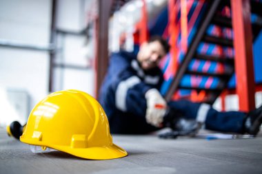 Safety at work. Close up view on hardhat and injured factory worker in background.