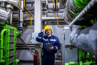 Caucasian industrial serviceman checking gas generators for electricity in heating plant.