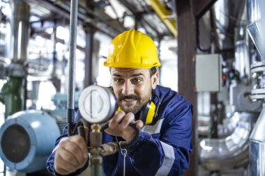Heating plant worker checking water temperature and pressure in boiler room.