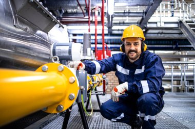 Professional refinery worker with hardhat standing by natural gas pipe. Oil and gas industry production.