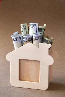konsept - rulo dolar banknotları el sanatları arka planında izole ahtan bir evin maketinde yatıyor
