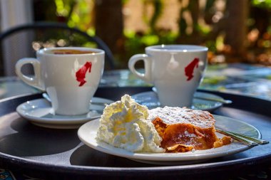 Elma ve kremalı bisküvi, güneşli bir günde açık bir kafede, iki beyaz fincan kahve ve kakaonun yanında duruyor.
