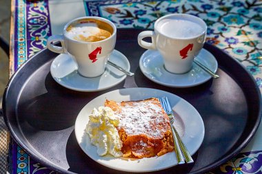 Elma ve kremalı bisküvi, güneşli bir günde açık bir kafede, iki beyaz fincan kahve ve kakaonun yanında duruyor.