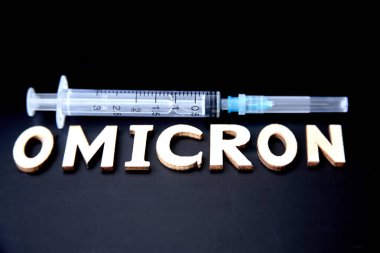 Ahşap harflerden yapılmış omikron kelimesi, siyah arka planda şırınga. Tıbbi konsept - Mutasyona uğramış koronavirüs SARS-CoV-2 grip salgını