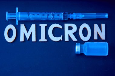 Ahşap harflerden, şırıngadan ve siyah arka planda tıbbi enjeksiyon şişesinden yapılmış omikron kelimesi. Tıbbi konsept - Mutasyona uğramış koronavirüs SARS-CoV-2 grip salgını