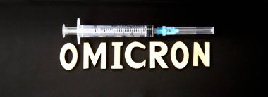 Ahşap harflerden yapılmış omikron kelimesi, siyah arka planda şırınga. Tıbbi konsept - Mutasyona uğramış koronavirüs SARS-CoV-2 grip salgını
