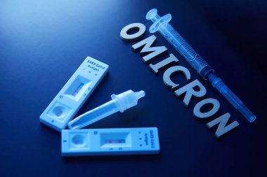 Omicron kelimesi ahşap harfler, şırınga, tıbbi enjeksiyon şişesi ve 2 covid-19 antijen testinden pozitif sonuç çıktı. Konsept-mutasyona uğramış koronavirüs SARS-CoV-2 grip salgını.