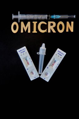 Omicron kelimesi ahşap harfler, şırınga, tıbbi enjeksiyon şişesi ve 2 covid-19 antijen testinden pozitif sonuç çıktı. Konsept-mutasyona uğramış koronavirüs SARS-CoV-2 grip salgını.
