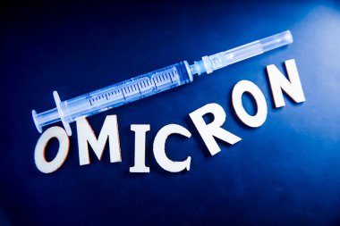 Ahşap harflerden yapılmış omikron kelimesi, siyah arka planda şırınga. Tıbbi konsept - Mutasyona uğramış koronavirüs SARS-CoV-2 grip salgını