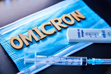 Omicron kelimesi ahşap harfler, şırınga ve 2 covid-19 antijen testinden yapılmış. Siyah arka plan pozitif. Konsept mutasyona uğramış koronavirüs SARS-CoV-2 grip salgını