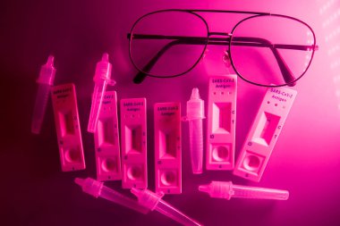 5 covid-19 antijen testi pozitif, tampon şişeler ve koyu kırmızı arka planda ince siyah çerçeveli gözlük. Kendi kendini test. Evde test edin. Corona, Coronavirus SARS-CoV-2 grip salgını