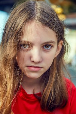 Kırmızı kazaklı, tatminsiz ve kızgın genç bir kızın dikey görüntüsü ve canı sıkkın, güneşli bir gün. Negatif insan yüz ifadeleri ve tepkileri