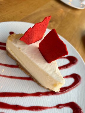 Ahududu ya da çilek reçeli serpilmiş beyaz bir tabakta beyaz bir fincan kahvenin yanında cheesecake.