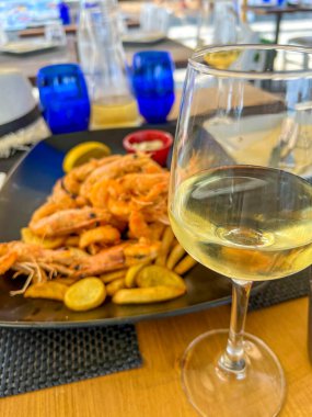 Izgara büyük kral karidesleri siyah bir tabakta patates kızartmasının üzerinde bir dilim limon ve sos ile uzanır.