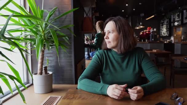 Hübsche Frau sitzt im Café und redet. Grünes Kleid mit langen Ärmeln — Stockvideo